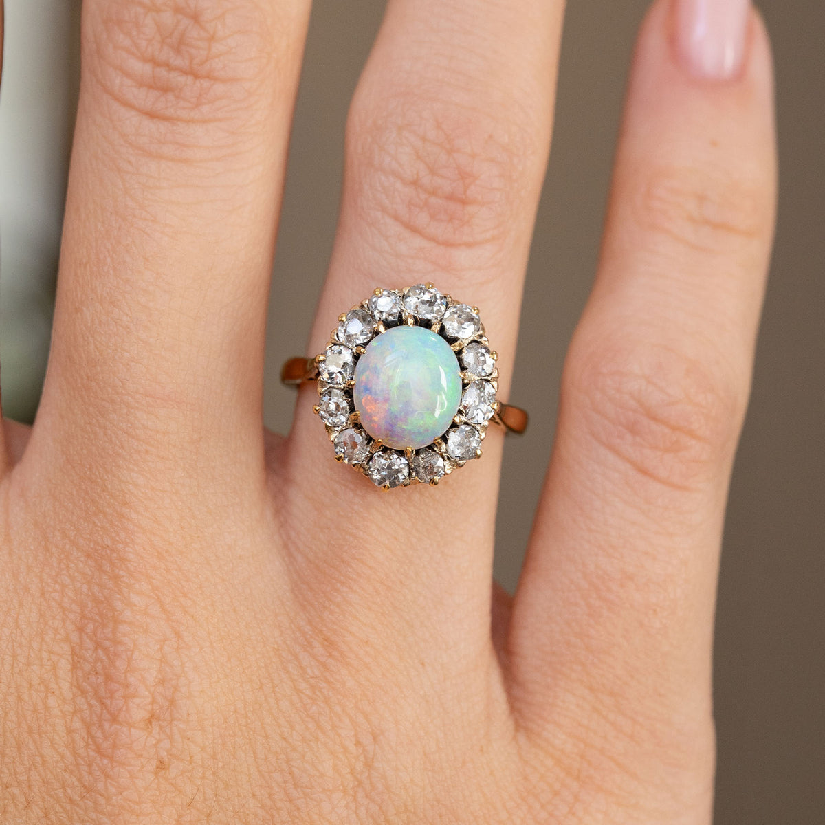 Detailed hand shot highlighting the luminous oval opal, antique diamond surround and warm yellow gold setting.
