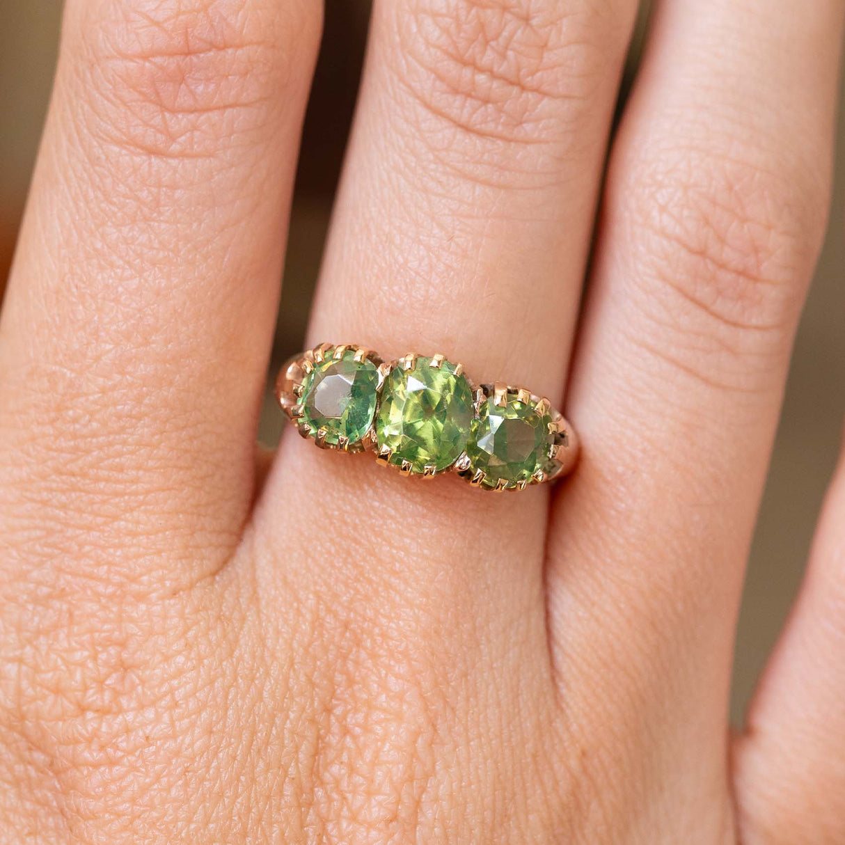 A close up picture of a green zircon trilogy ring in gold worn on the hand to show details.