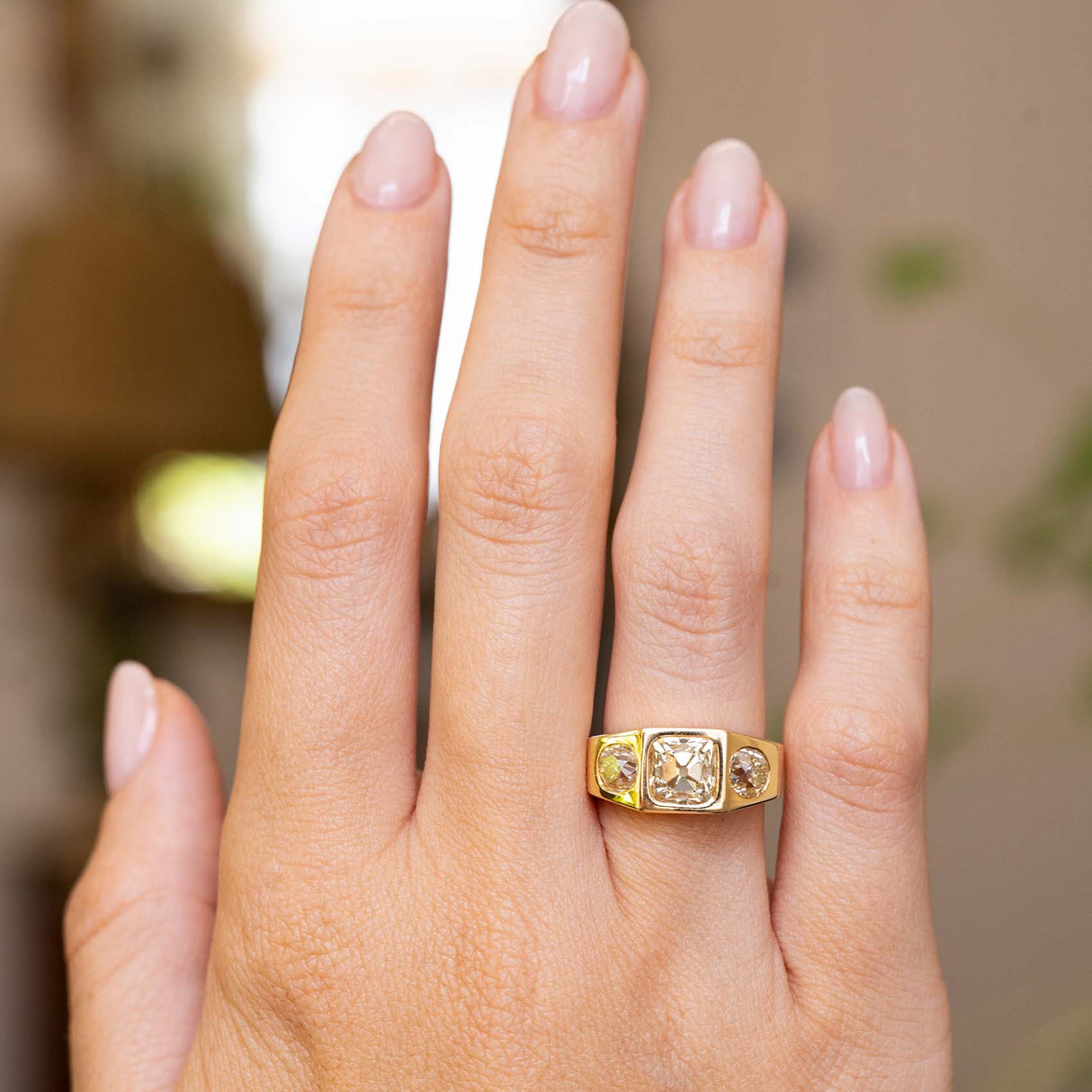 A hand wearing a yellow gold Vintage, 1970s Peruzzi cut diamond three-stone gypsy ring seen from a distance