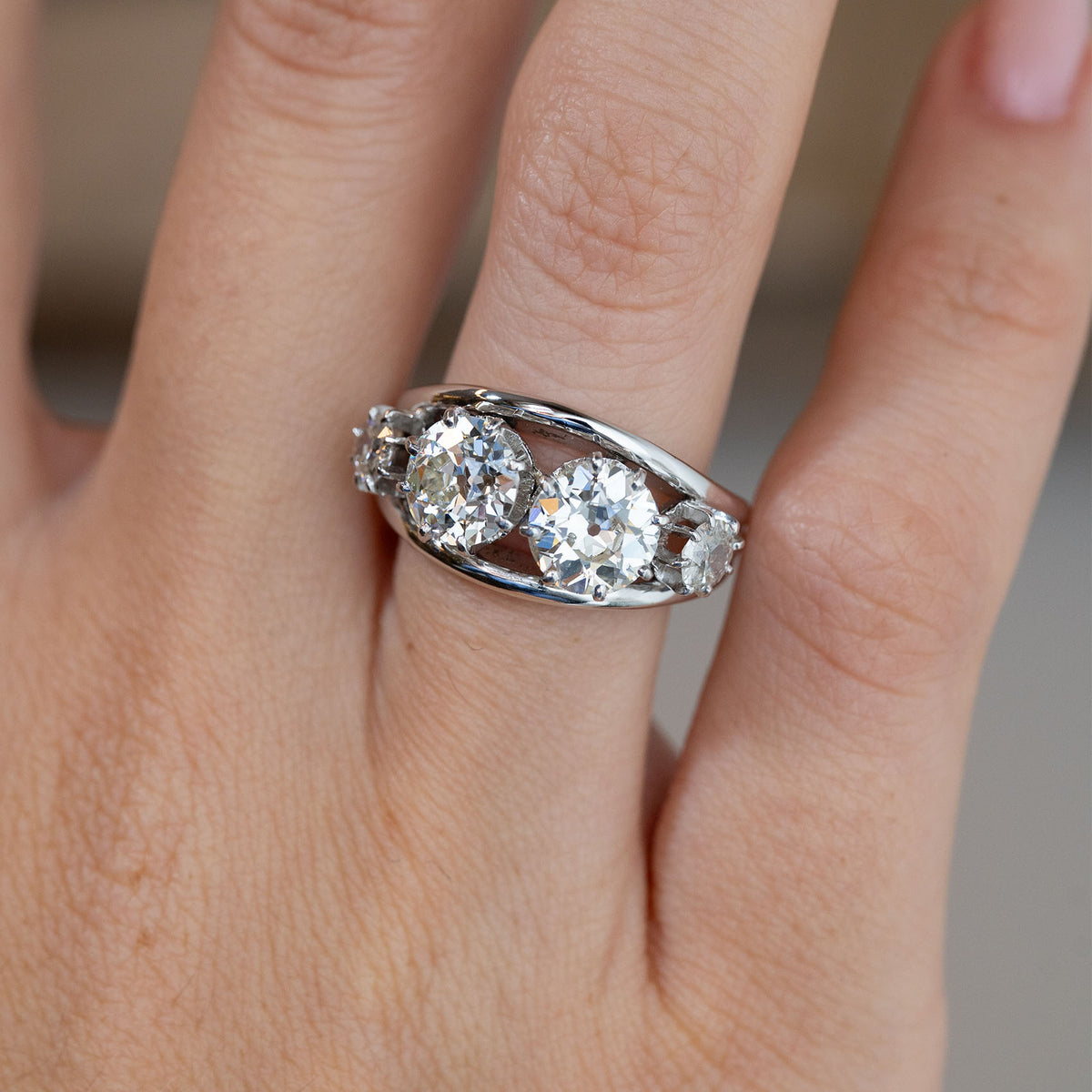 Close-up of the four-stone diamond engagement ring on a finger, featuring two prominent round old-cut diamonds in an openwork setting.