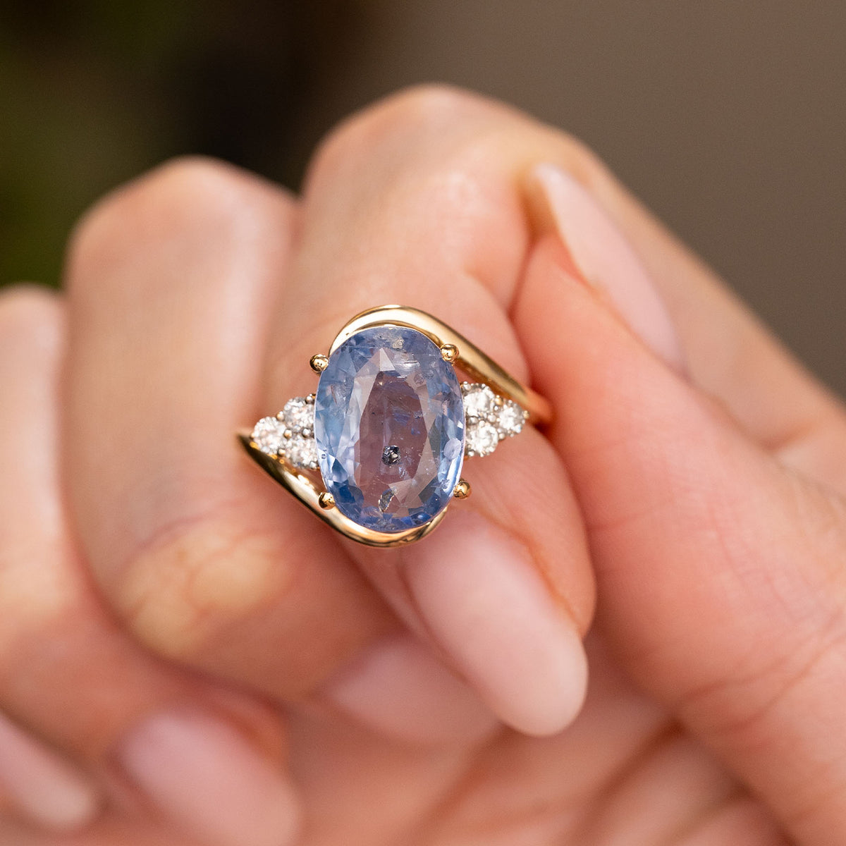 Fingers holding a Vintage, 1990s Blue sapphire and diamond three-stone ring in yellow gold