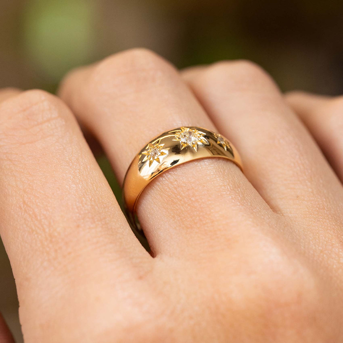 A close-up of a hand wearing an Antique, Edwardian diamond three-stone gypsy ring in yellow gold shown from a low angle to display that the diamonds are set in flush with the band.