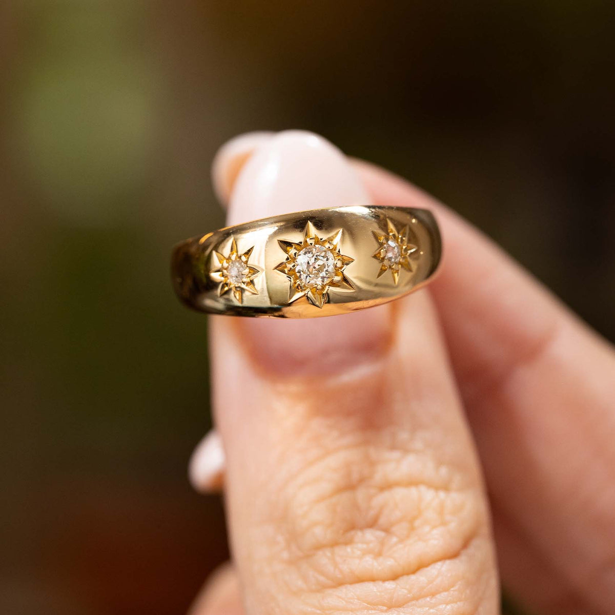 Antique, Edwardian diamond three-stone gypsy ring with three old cut diamonds set in engraved stars on a yellow gold band held between the fingers and close to the camera