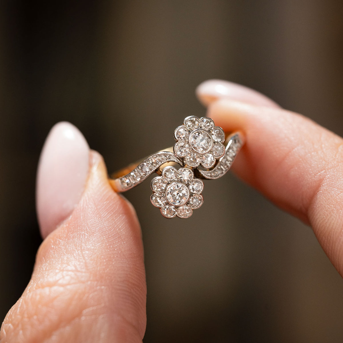 An antique Edwardian double diamond cluster two stone engagement ring in yellow gold held in between the fingers to give a detailed view of the style and setting.