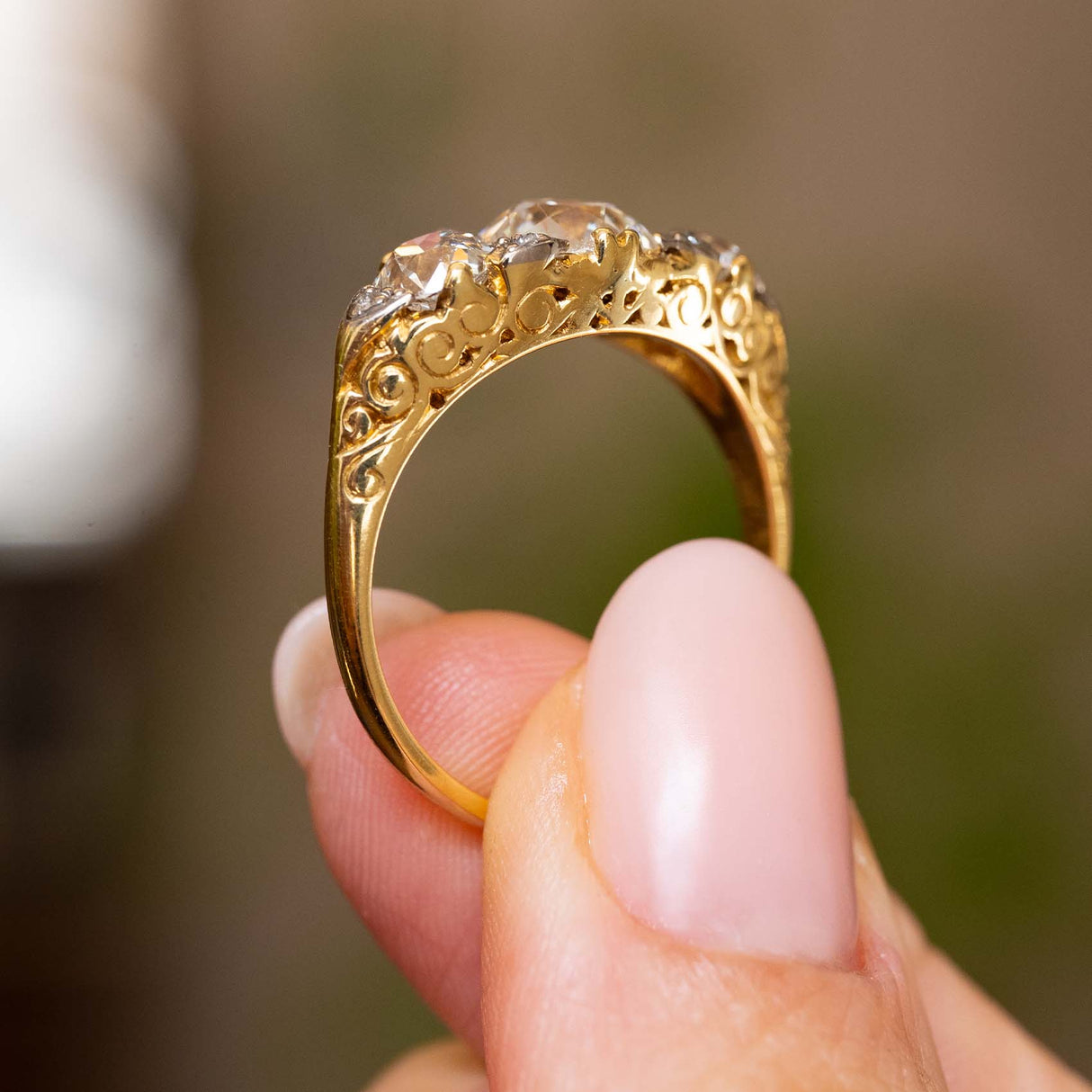Rear view of the Victorian ring held between two fingers, showing the ornate openwork gallery tapering into a solid 18ct yellow gold band.