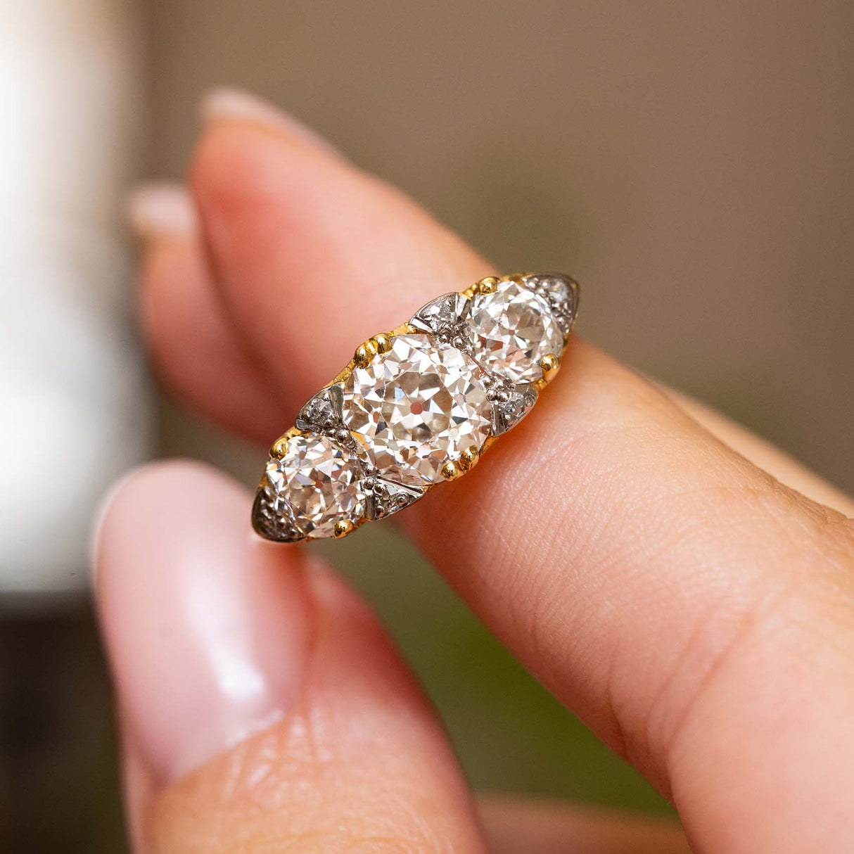 Angled close-up of the Victorian ring held between two fingers, showcasing the large cushion-shaped centre diamond and graduated old-cut side stones.
