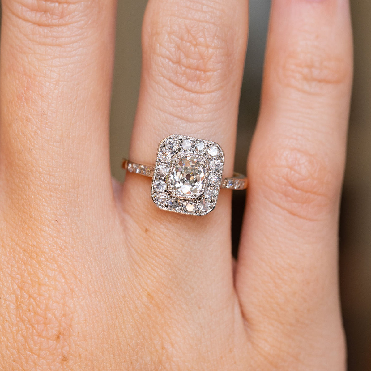 Close-up of an antique old-mine diamond engagement ring worn on the finger, showing its geometric cluster and milgrain detailing.