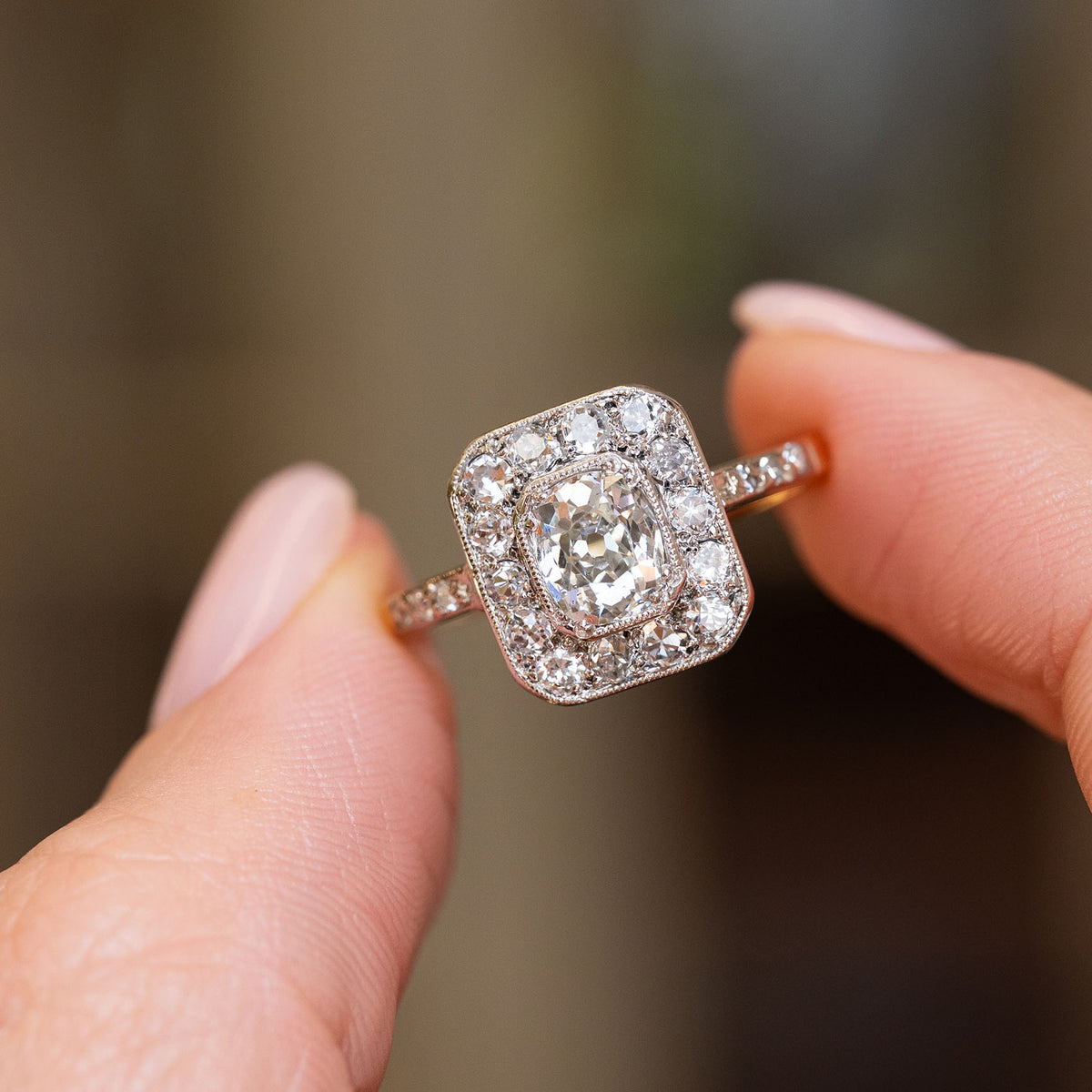 Antique Edwardian diamond cluster ring held between the fingers, showcasing the old-mine cut stones and diamond-set shoulders.