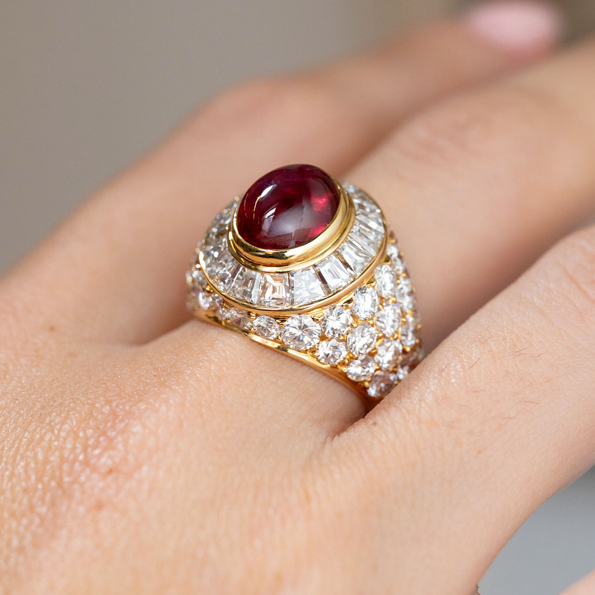 Side angle on the hand showing the raised cabochon ruby, concentric diamond surround and rounded bombé silhouette.