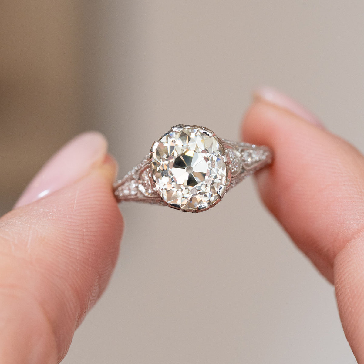 Old-mine diamond solitaire held between the fingers, offering a detailed look at its Edwardian craftsmanship.
