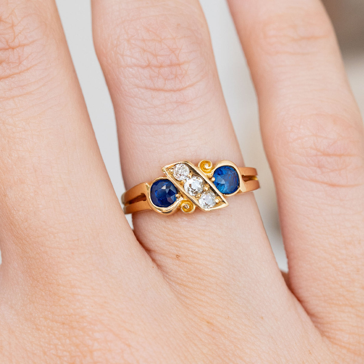 Detailed finger close-up showing three graduated old-mine cut diamonds crossing between two cushion-cut blue sapphires.