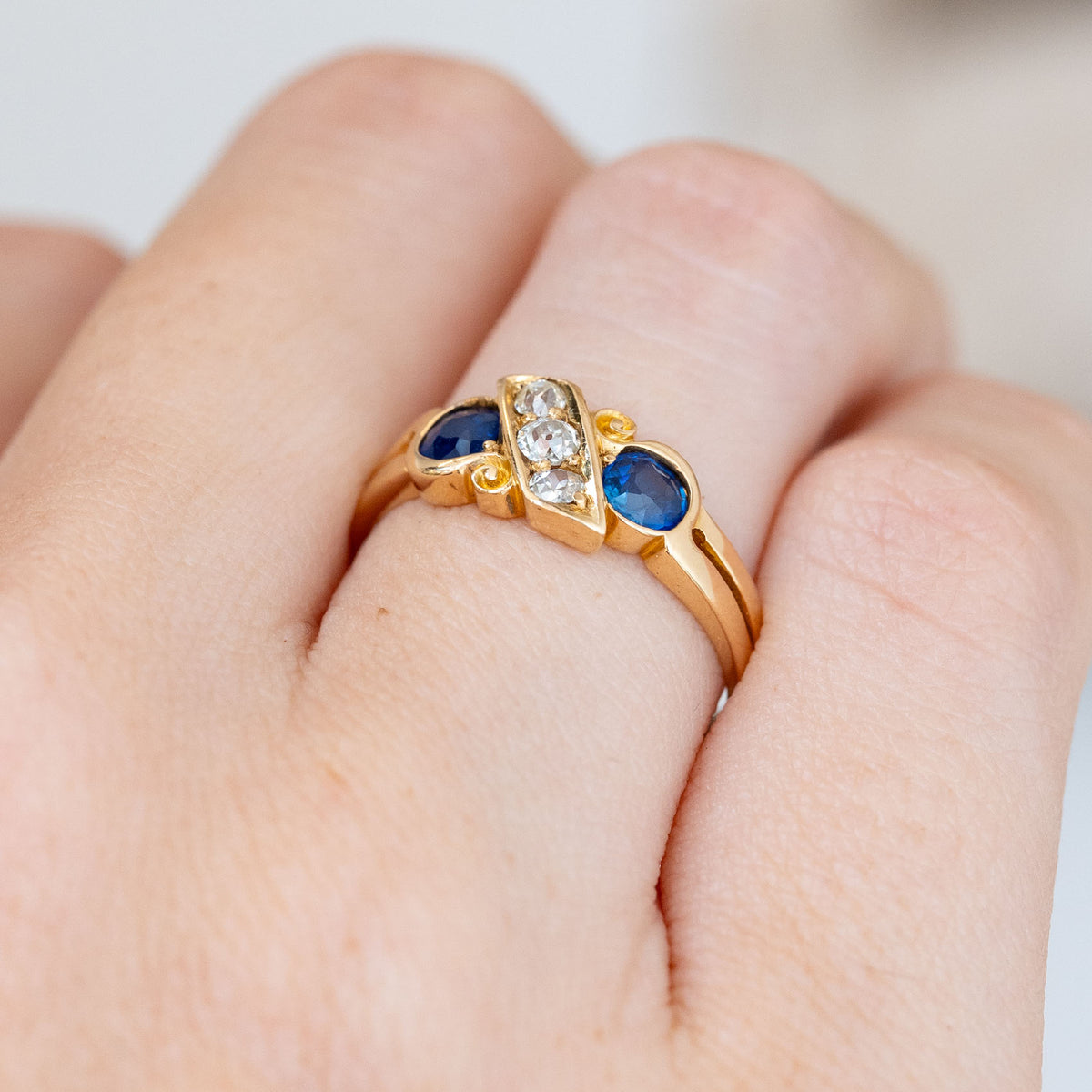 Seen obliquely, the antique ring reveals its split shoulders, raised gemstones and flowing scrollwork around the five-stone setting.