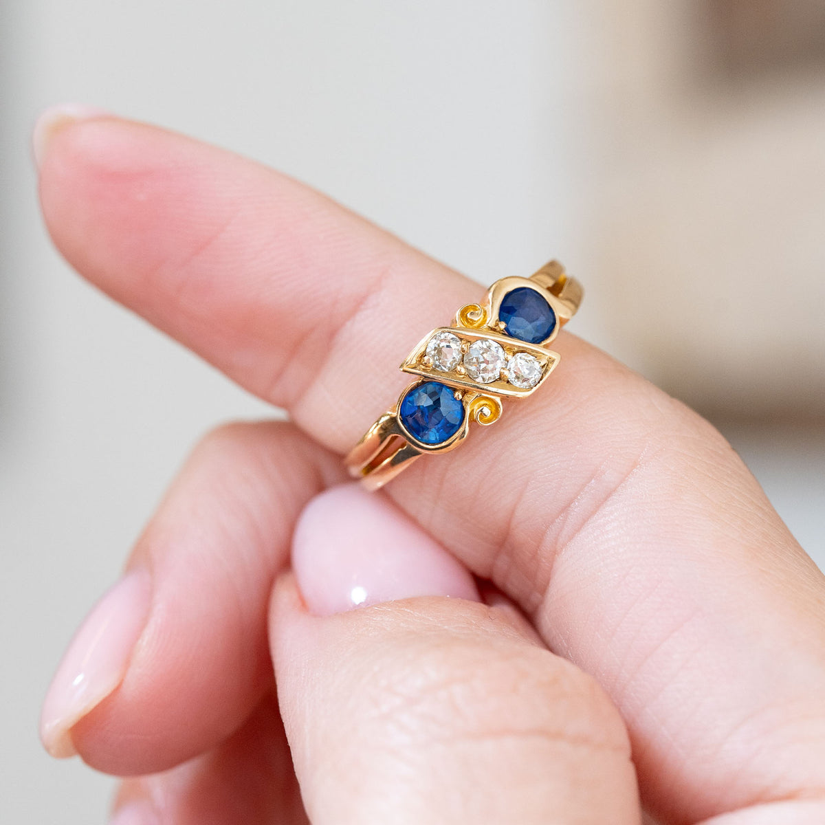 Held between the fingers, the ring’s bold blue sapphires frame a central line of softly faceted antique diamonds.