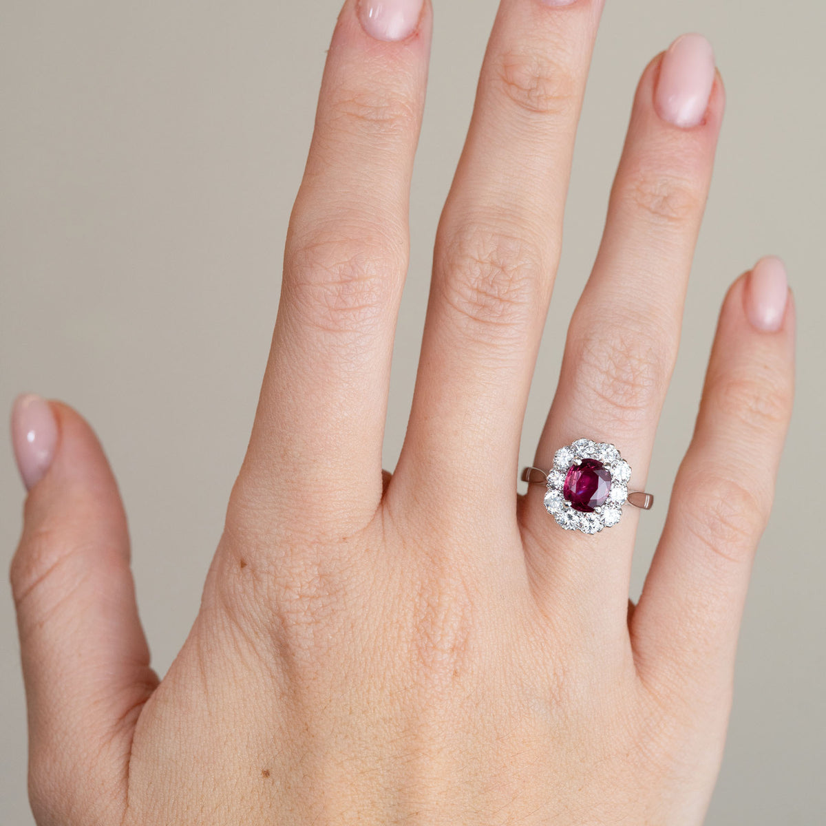 A 1960s ruby engagement ring worn on a hand, with a rich pinkish-red centre stone framed by a sparkling diamond surround.