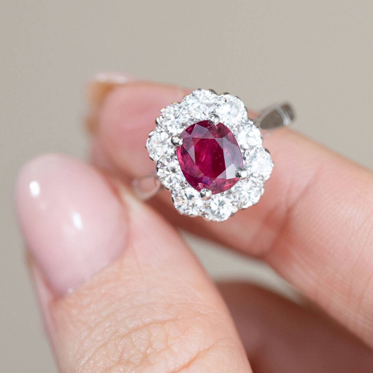 Detailed front-facing photograph of the vintage ruby halo ring held between fingertips, emphasising the contrast between the deep pink-red ruby and bright diamonds.