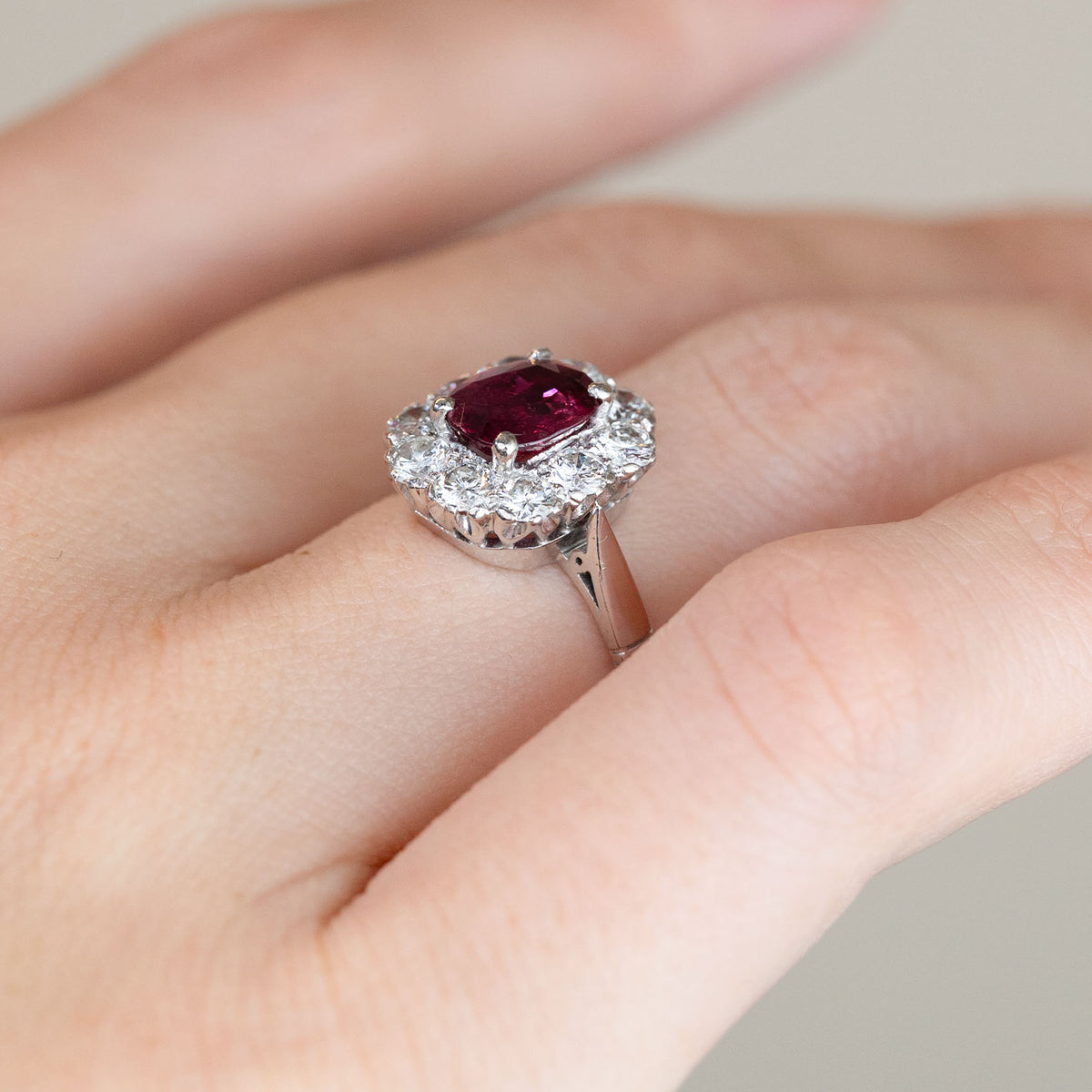 Angled view of the 1960s ruby and diamond engagement ring worn on a finger, displaying the raised cluster head and delicate white gold shoulders.