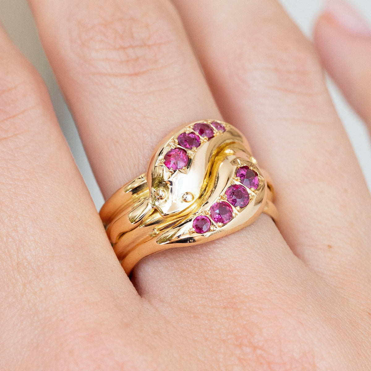 Close-up of the vintage Victorian ring worn on the finger, with two ruby-set snake heads crossing in yellow gold.