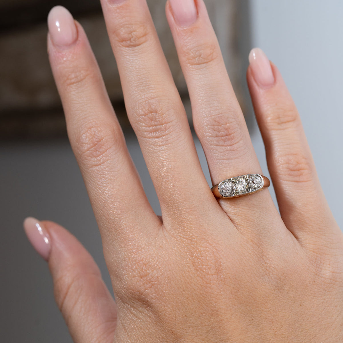 Antique Edwardian diamond three-stone engagement ring worn on a hand, displaying its three sparkling old-cut diamonds set horizontally across a wide yellow gold band.
