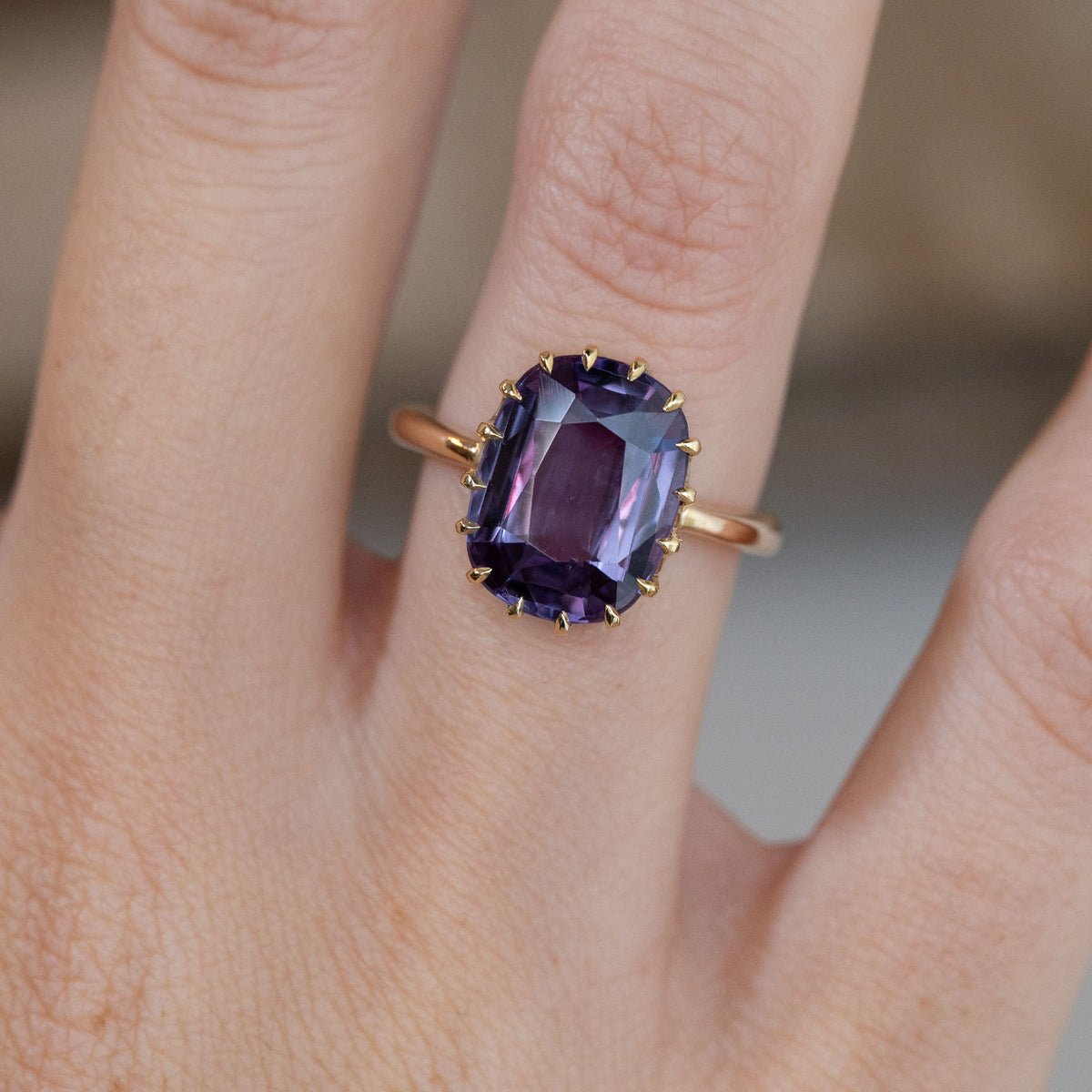 Close-up of the rectangular purple sapphire solitaire ring worn on a finger, featuring an intricate yellow gold claw setting.