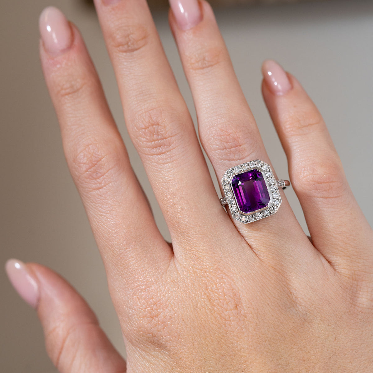 Antique Art Deco amethyst and diamond cluster ring worn on a hand, displaying its striking rectangular purple gemstone framed by sparkling diamonds in white gold.