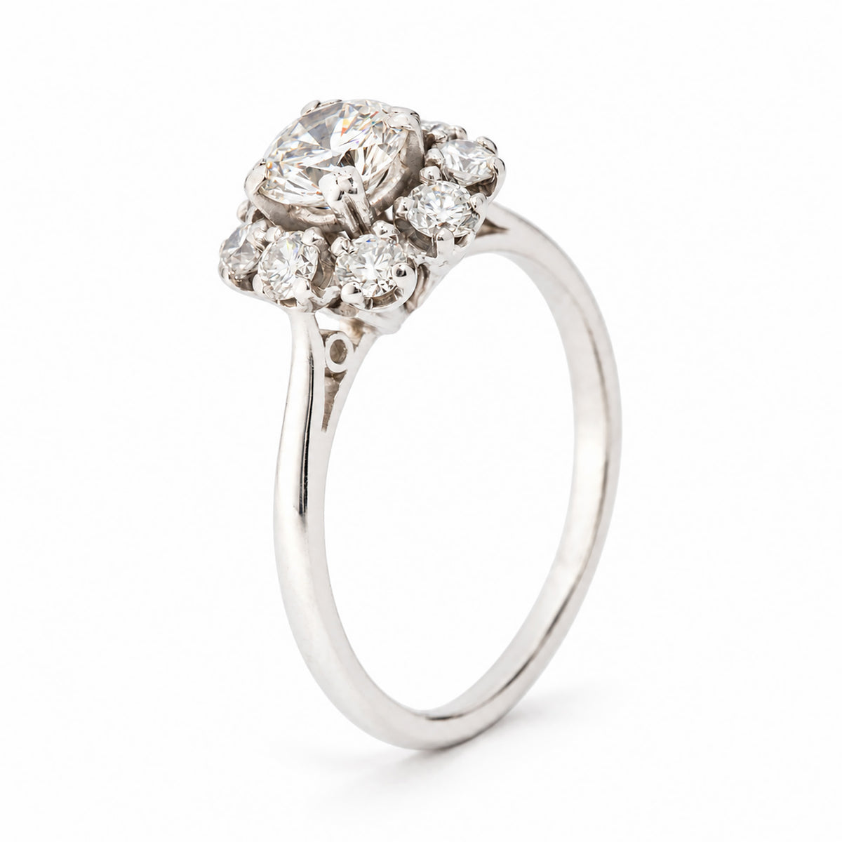 Angled studio view of a vintage 1950s diamond cluster engagement ring in white gold, showcasing its raised floral diamond setting, intricate claw details and polished band.