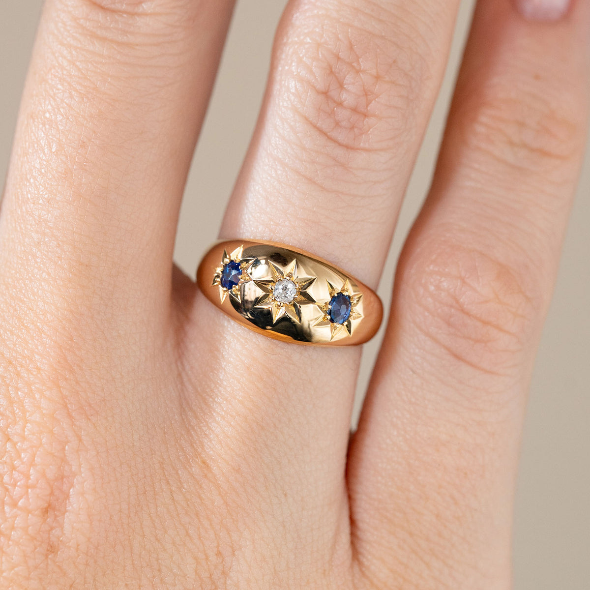 Close-up of the sapphire and diamond gypsy ring on a finger, revealing its intricate star-shaped settings and smooth gold finish.