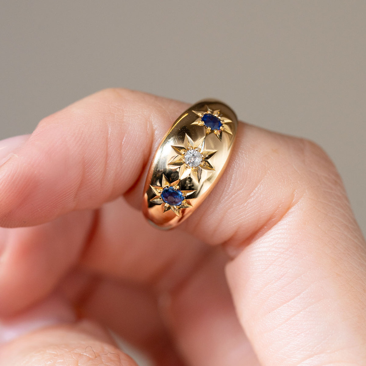 Detailed photograph of the antique gypsy ring held between fingers, highlighting the three gemstones nestled within ornate starburst settings.
