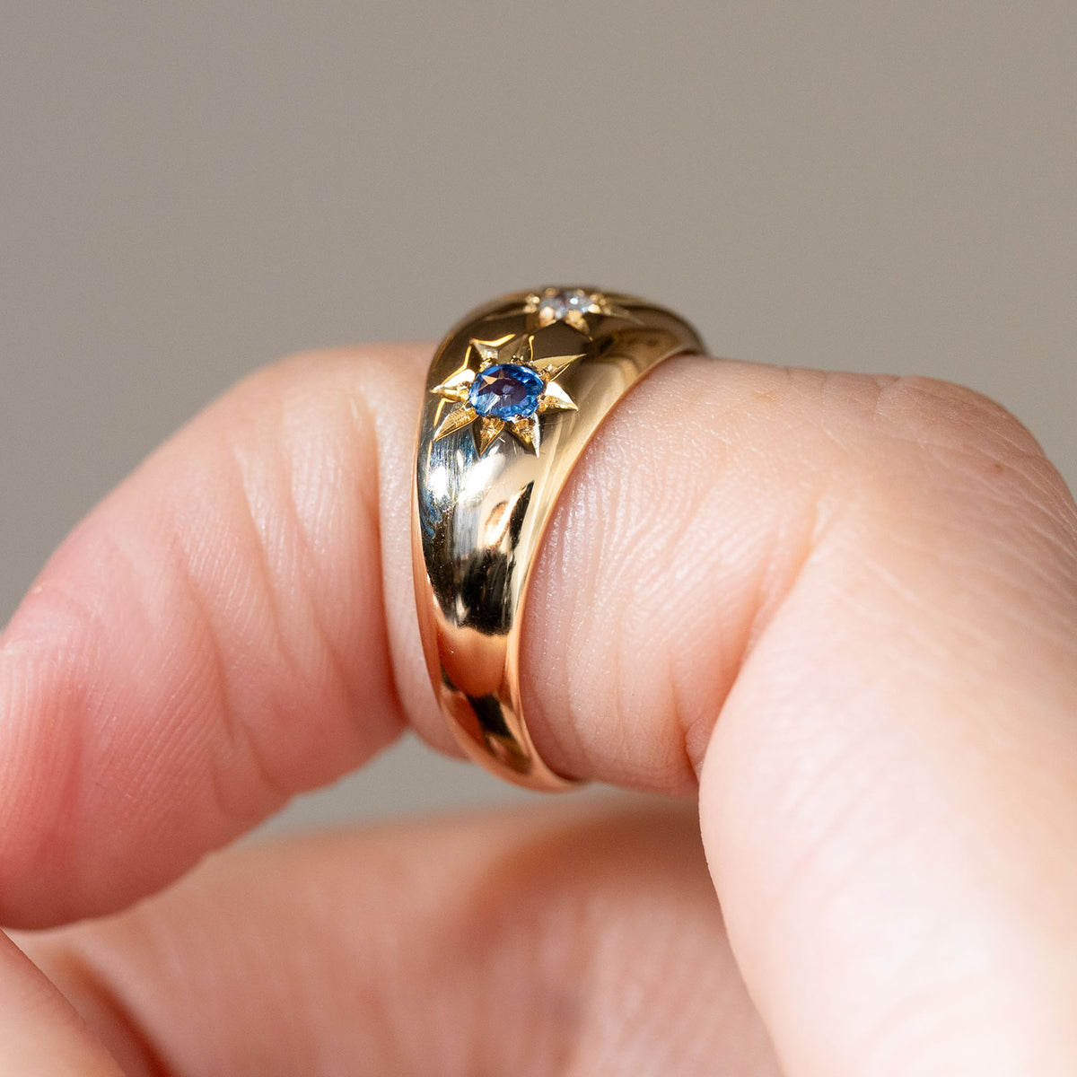 Side view of the Edwardian sapphire and diamond ring worn on a finger, displaying its substantial gold band and gently domed profile.