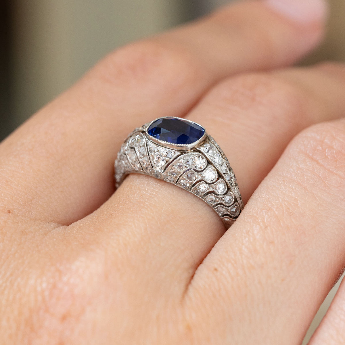 Elevated hand detail of a blue sapphire and rose-cut diamond bombé ring, highlighting its intricate platinum setting from the side.