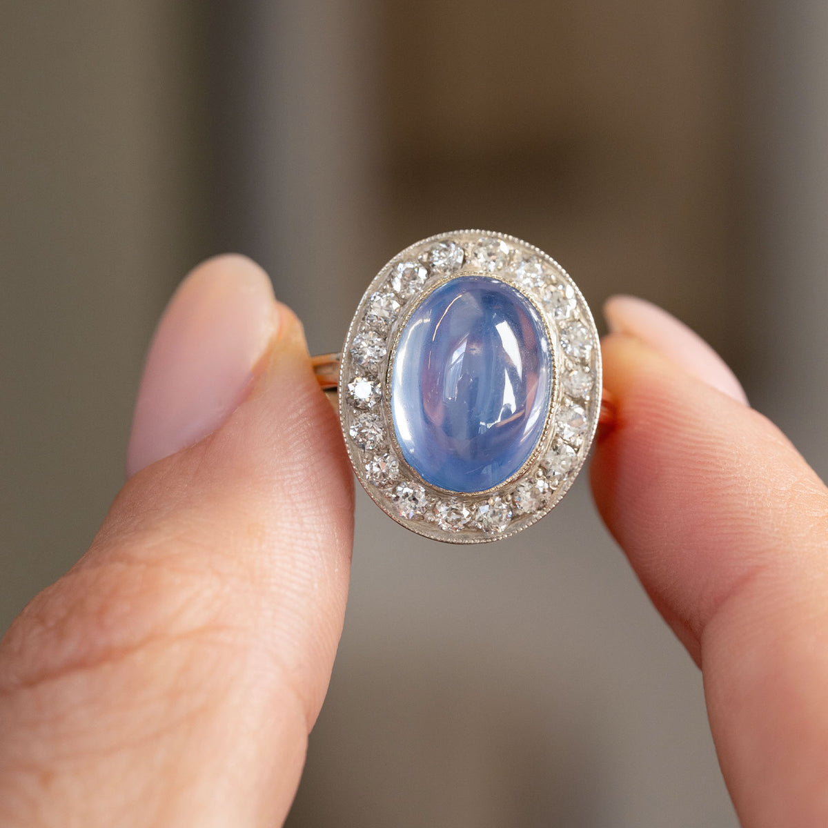 Handheld portrait of the oval cabochon sapphire framed by diamonds in a finely detailed silver and yellow gold setting.