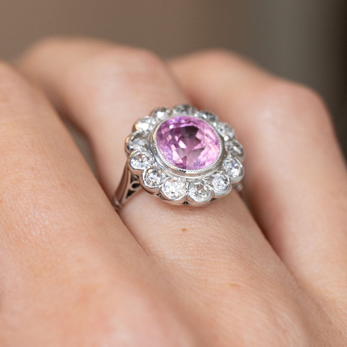 Angled on-hand view revealing the raised pink sapphire, scalloped diamond halo and sculptural setting.