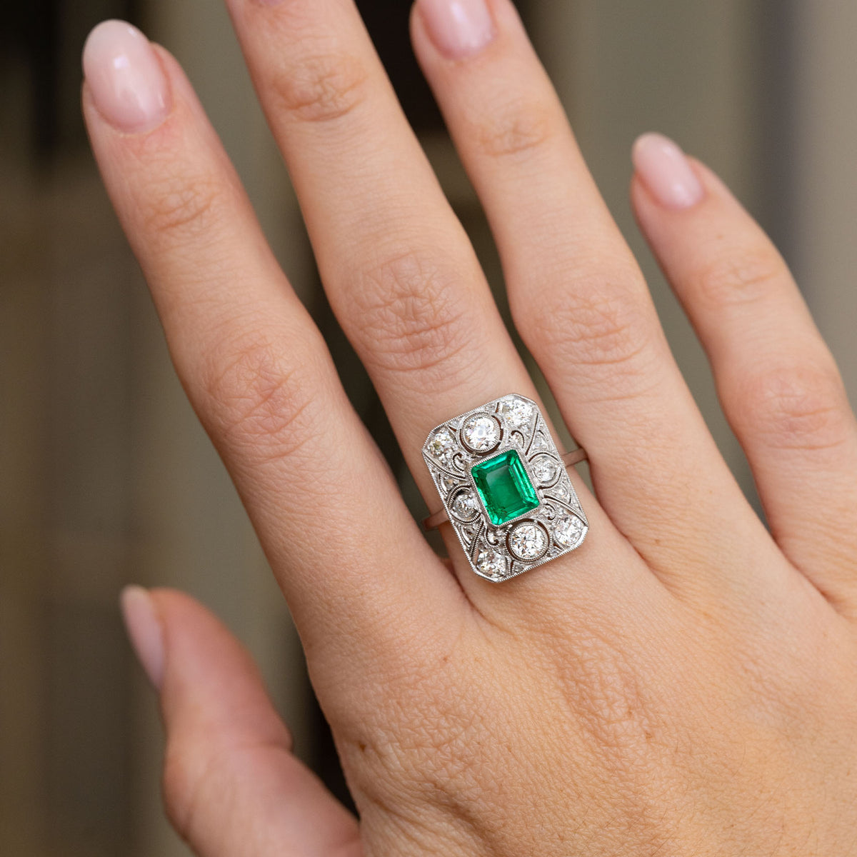 Art Deco emerald and diamond cluster ring worn on the hand, displaying its bold geometric proportions and fine platinum craftsmanship.