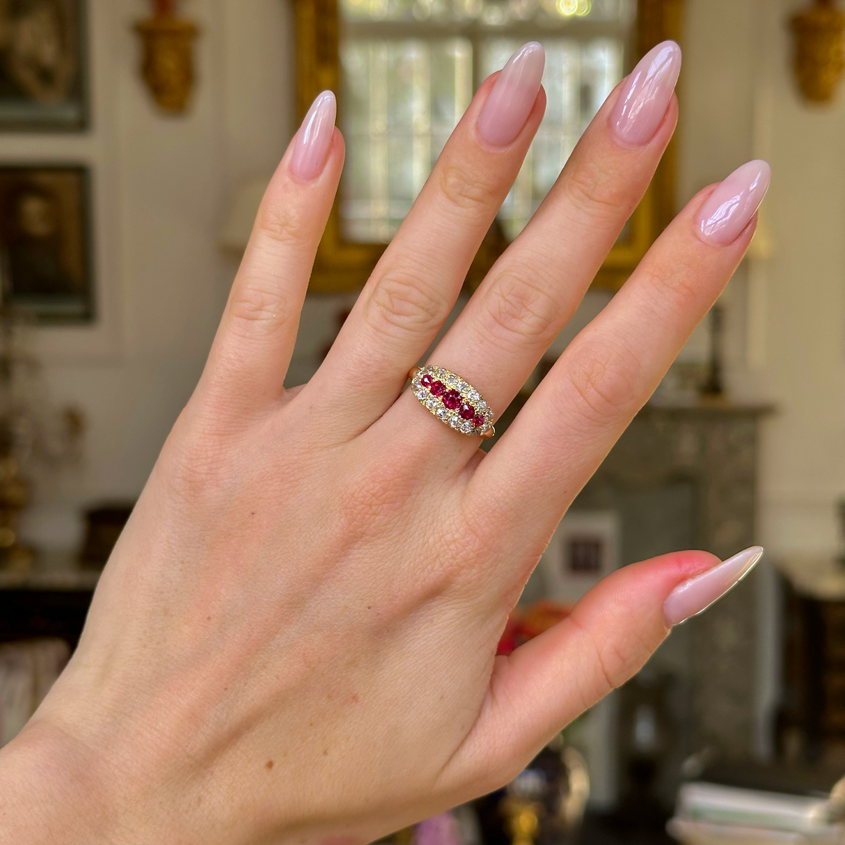 Ruby and diamond cluster engagement ring worn on hand.