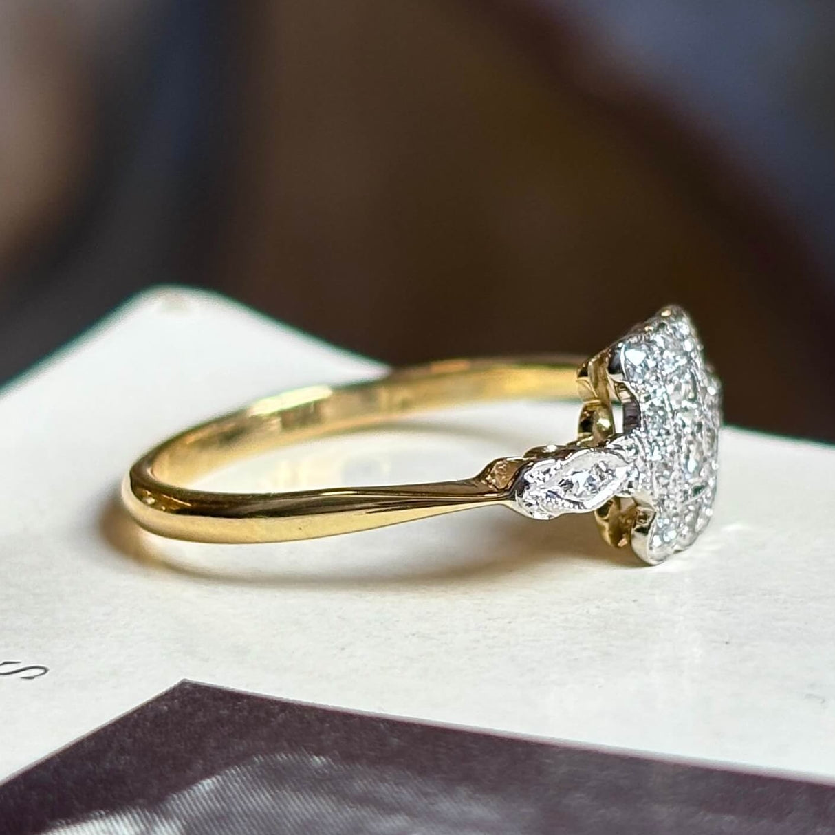 Antique, Edwardian diamond panel cluster engagement ring placed sideways on vintage book with blurred background