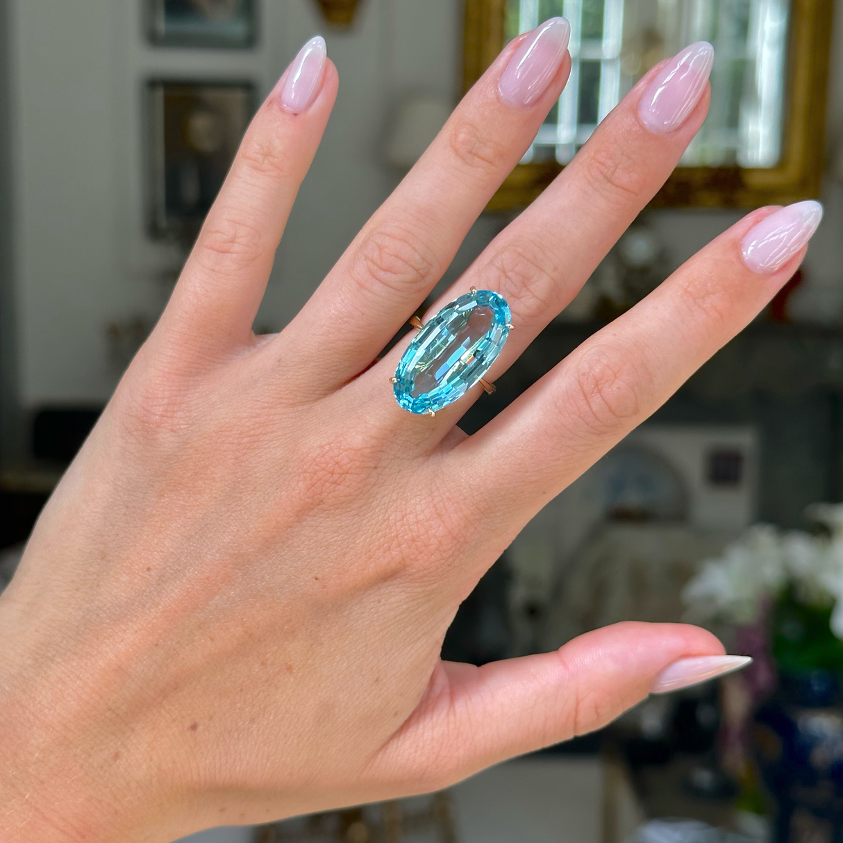 aquamarine and yellow gold cocktail ring on left hand, middle finger. Photographed with hand held up and antiquated bokeh background.