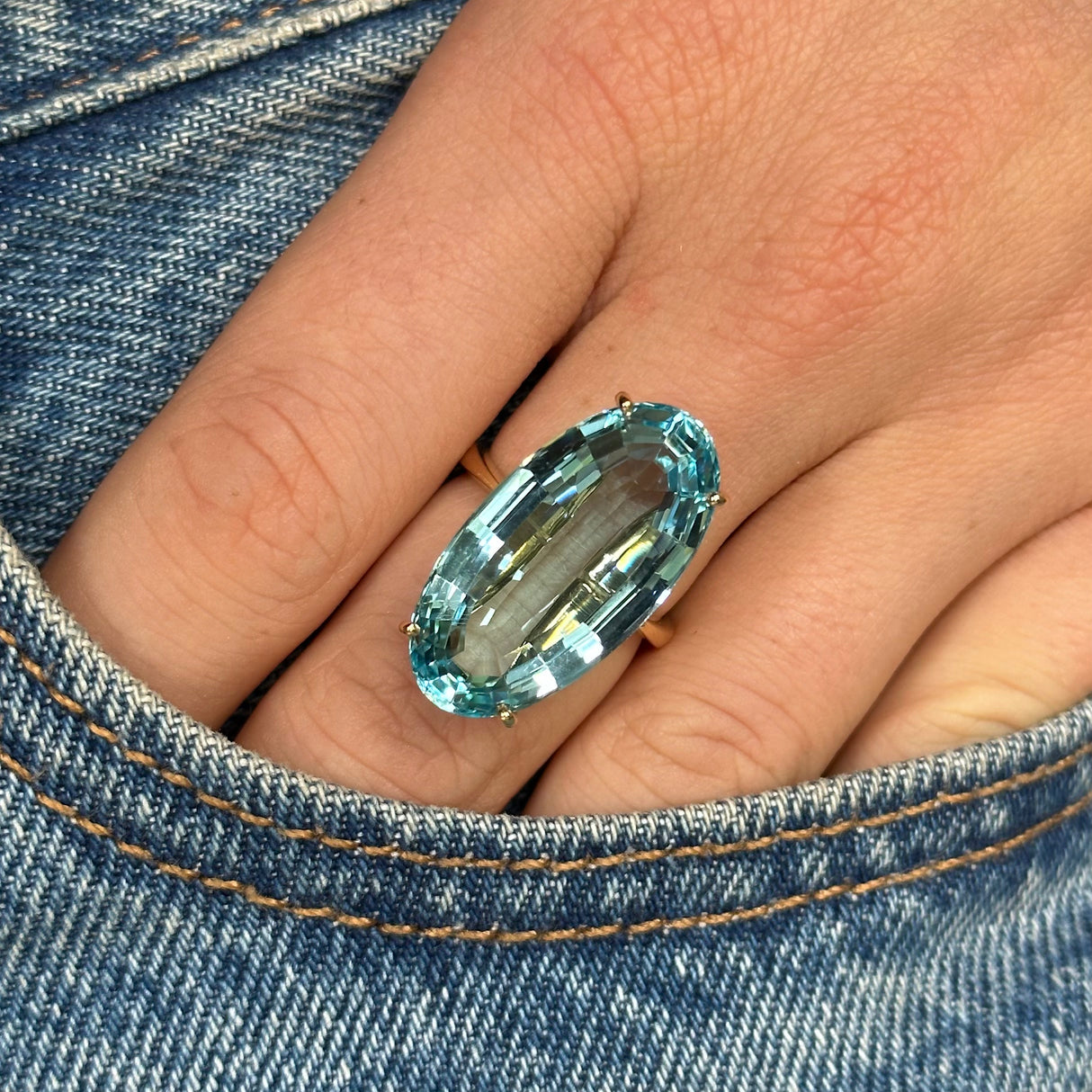 aquamarine and yellow gold cocktail ring on middle finger, photographed up close with hand tucked into pocket of blue denim jeans.