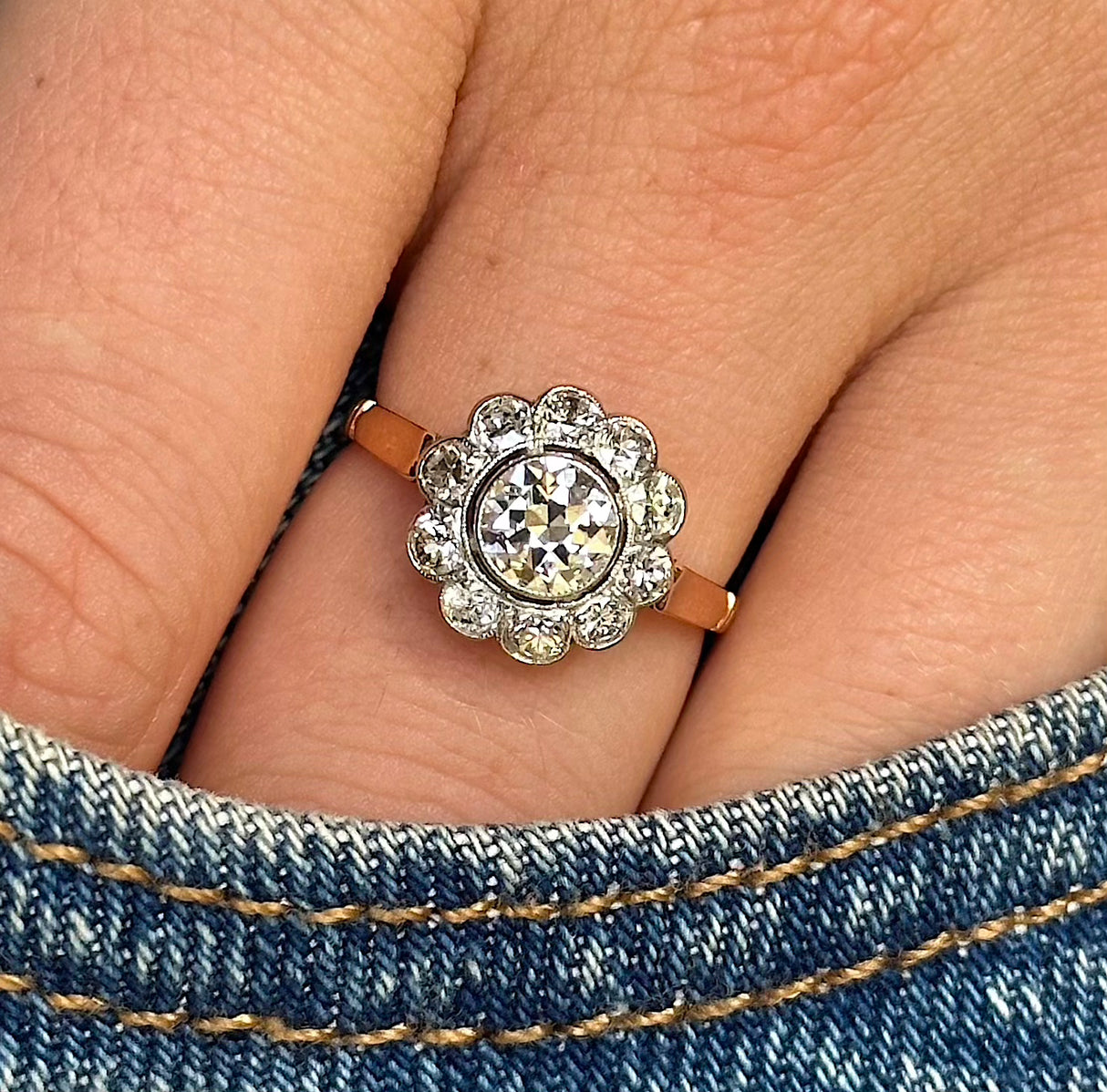 antique diamond cluster engagement ring, worn on hand and placed in pocket of denim jeans, front view.