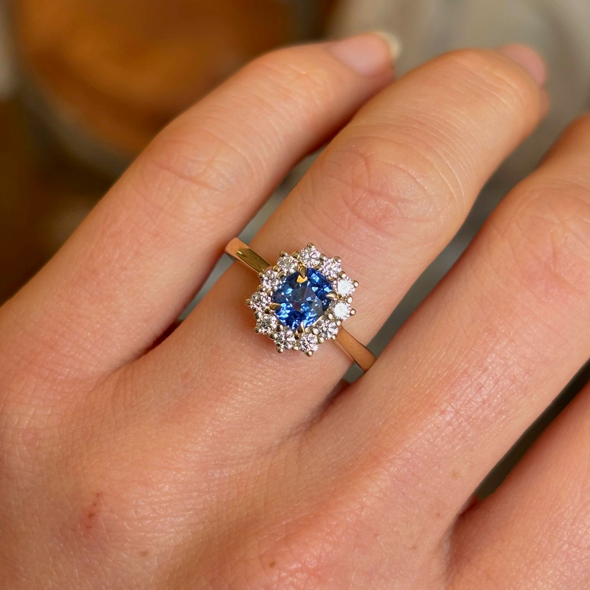 Blue sapphire and diamond cluster yellow gold engagement ring worn on hand close up