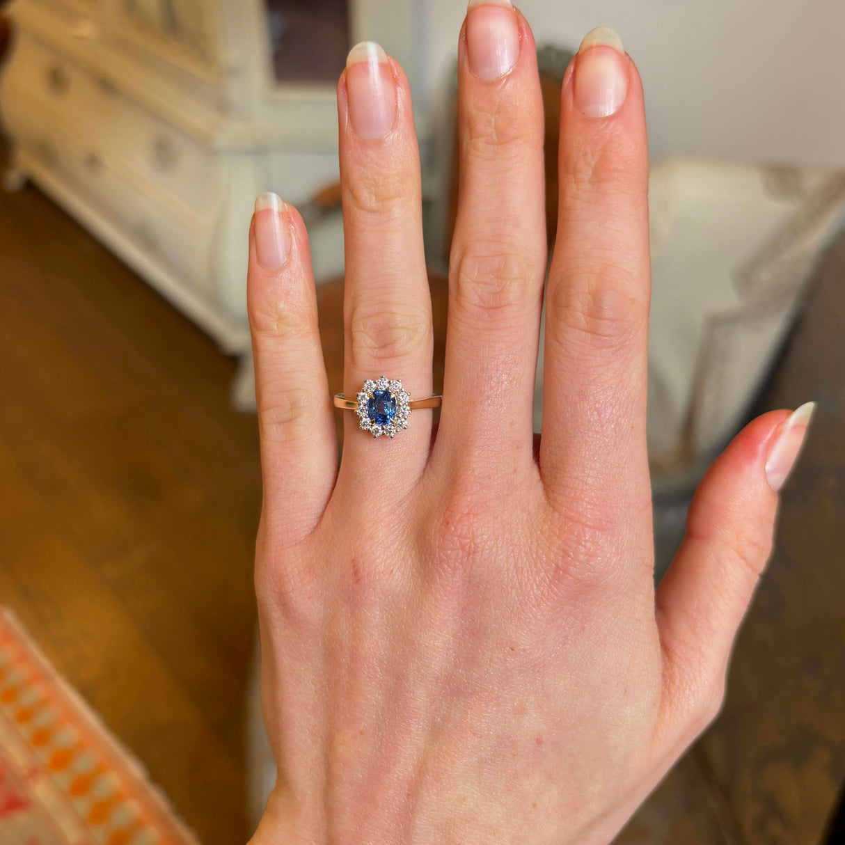Blue sapphire and diamond cluster engagement ring worn on hand showing perspective