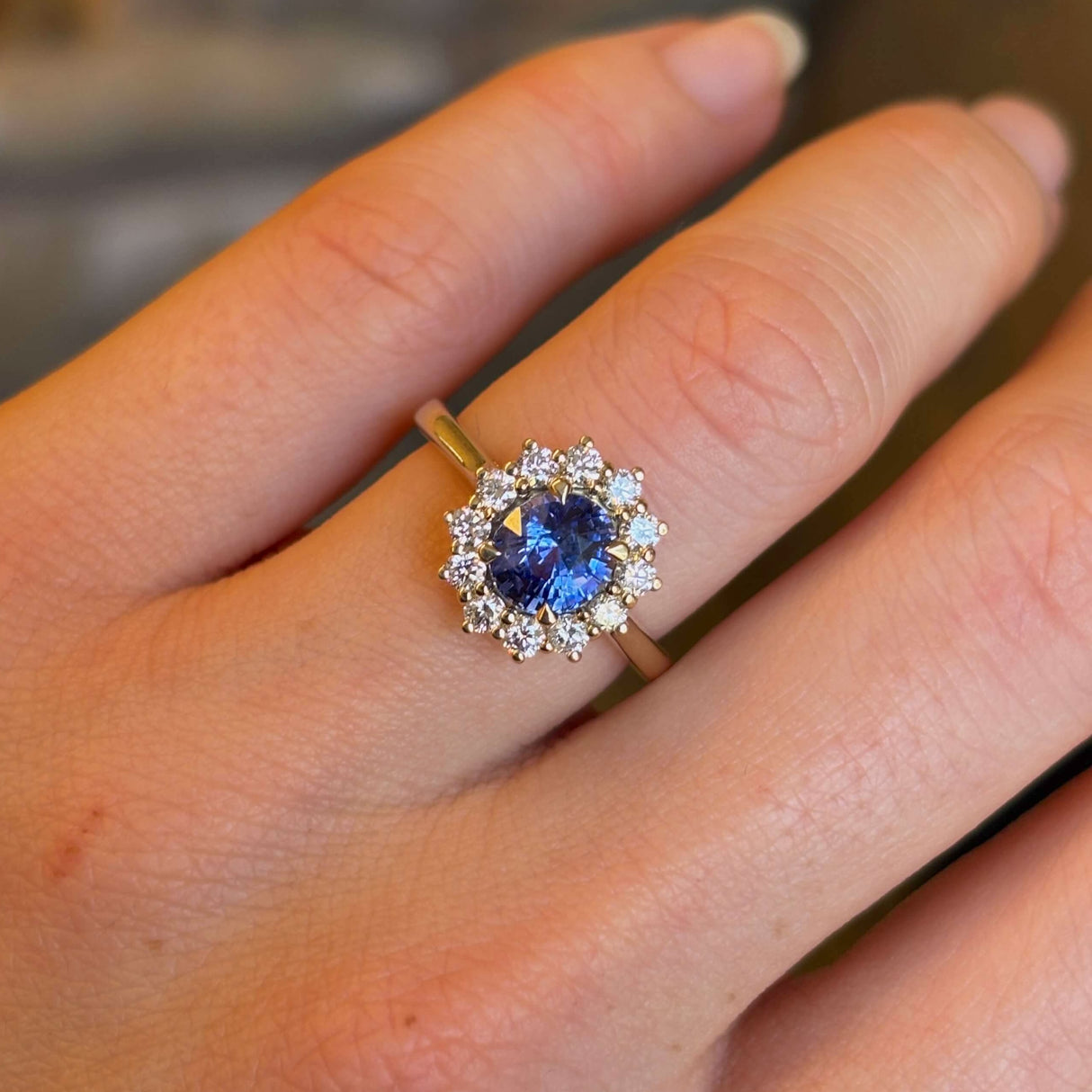 Blue sapphire and diamond cluster engagement ring worn on hand to show scale and proportion.