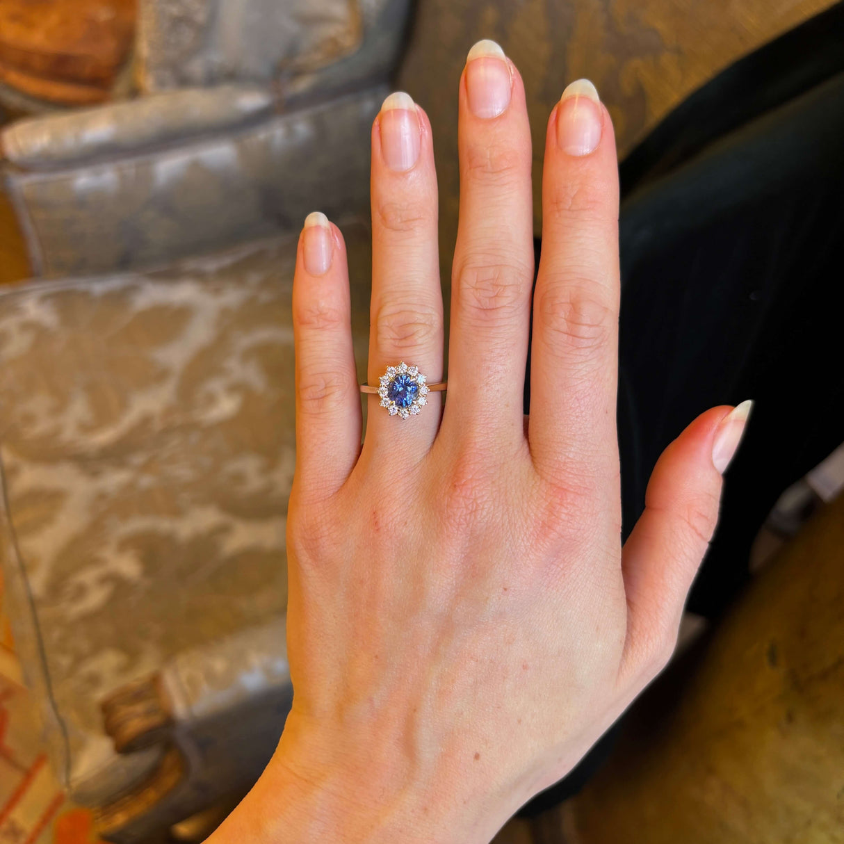 Blue sapphire and diamond cluster engagement ring worn on ring finger of left hand.