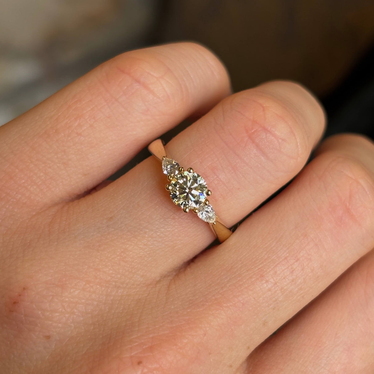 Round cut and pear-cut diamond three-stone yellow gold engagement ring close up on hand.