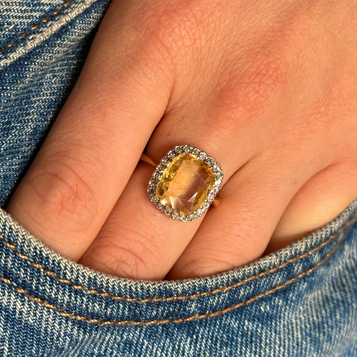 Yellow sapphire and diamond cluster ring, worn on hand placed in pocket of jeans, front view.