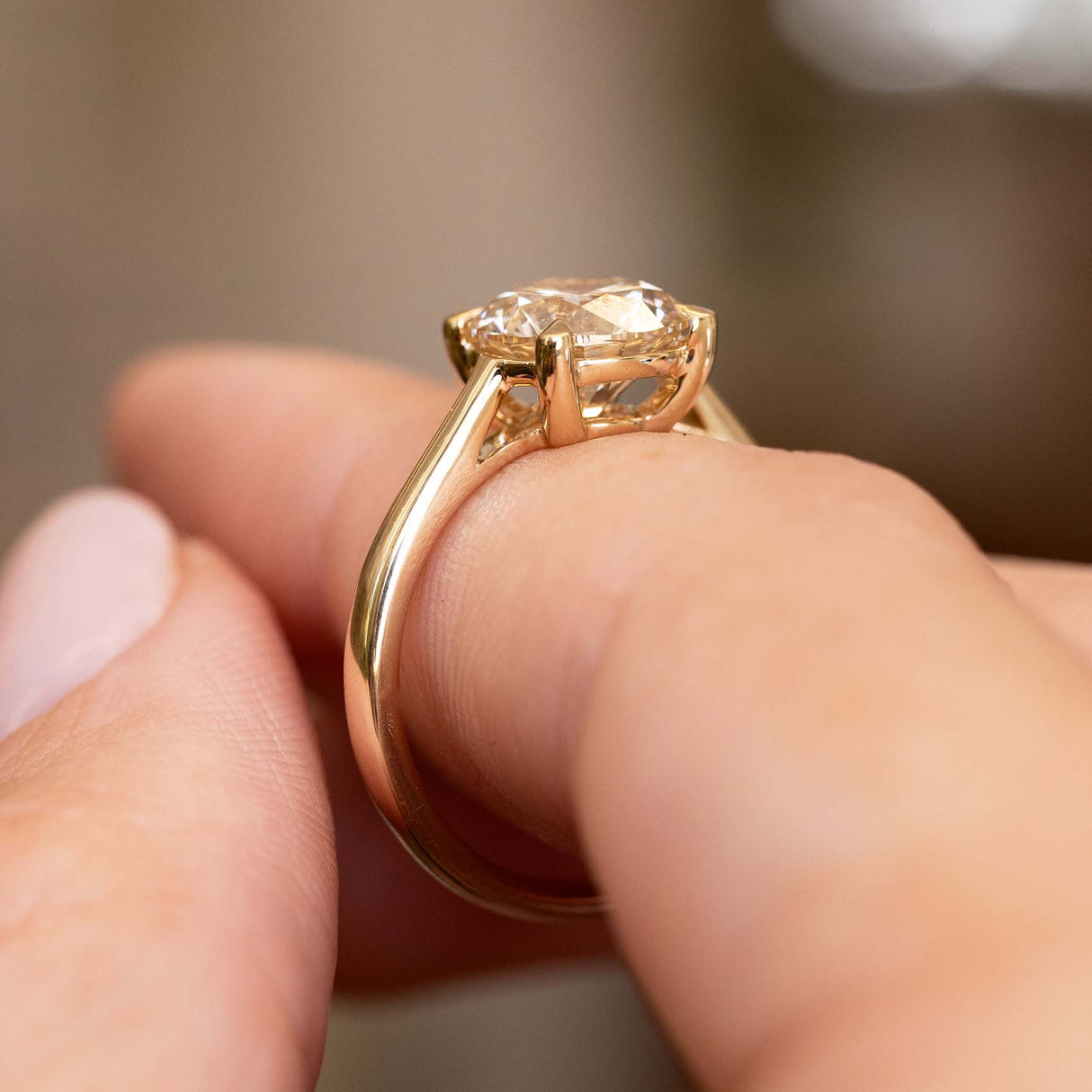 A close-up shot of a gold ring with round-cut light brown diamond being worn on a finger.