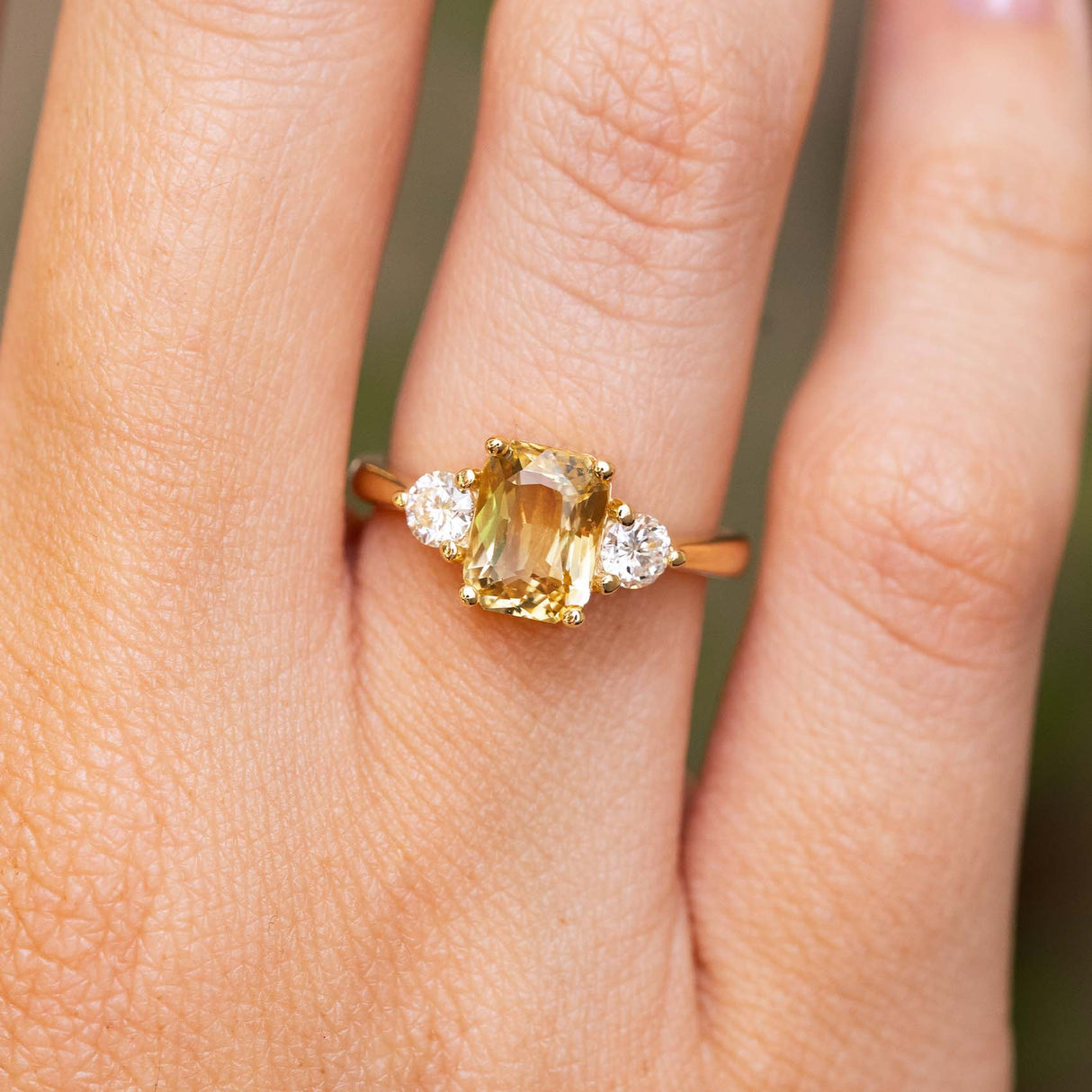 A close-up of a Antique-inspired, Yellow sapphire and diamond three-stone engagement ring in yellow gold, worn on a finger.