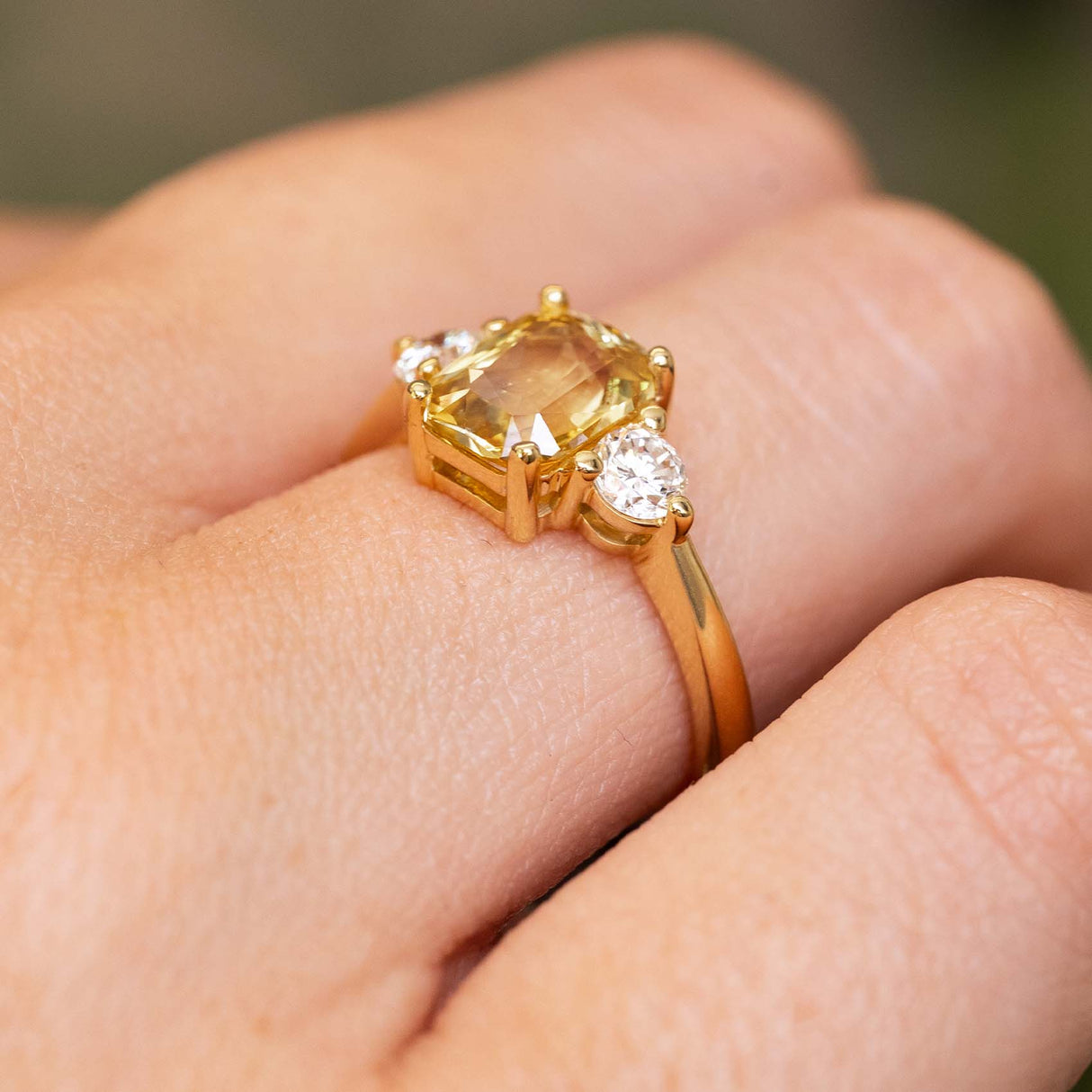 A close-up of a gold ring Antique-inspired, Yellow sapphire and diamond three-stone engagement ring worn on a person's finger shown from an angle to show the claw setting style