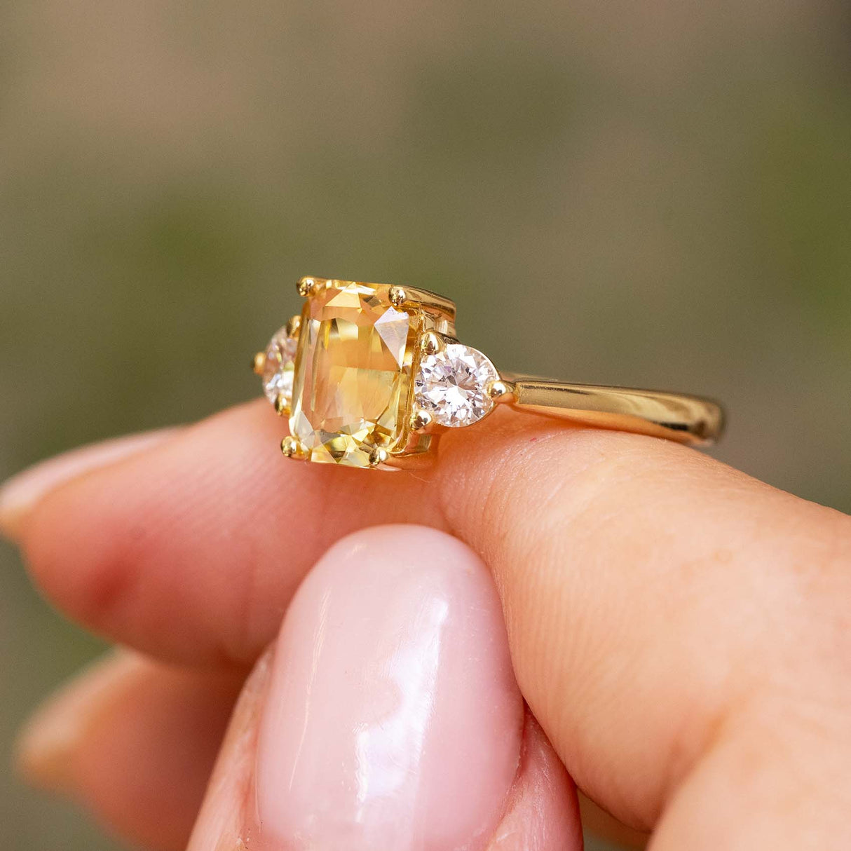 An Antique-inspired, Yellow sapphire and diamond three-stone engagement ring balanced on a persons finger.