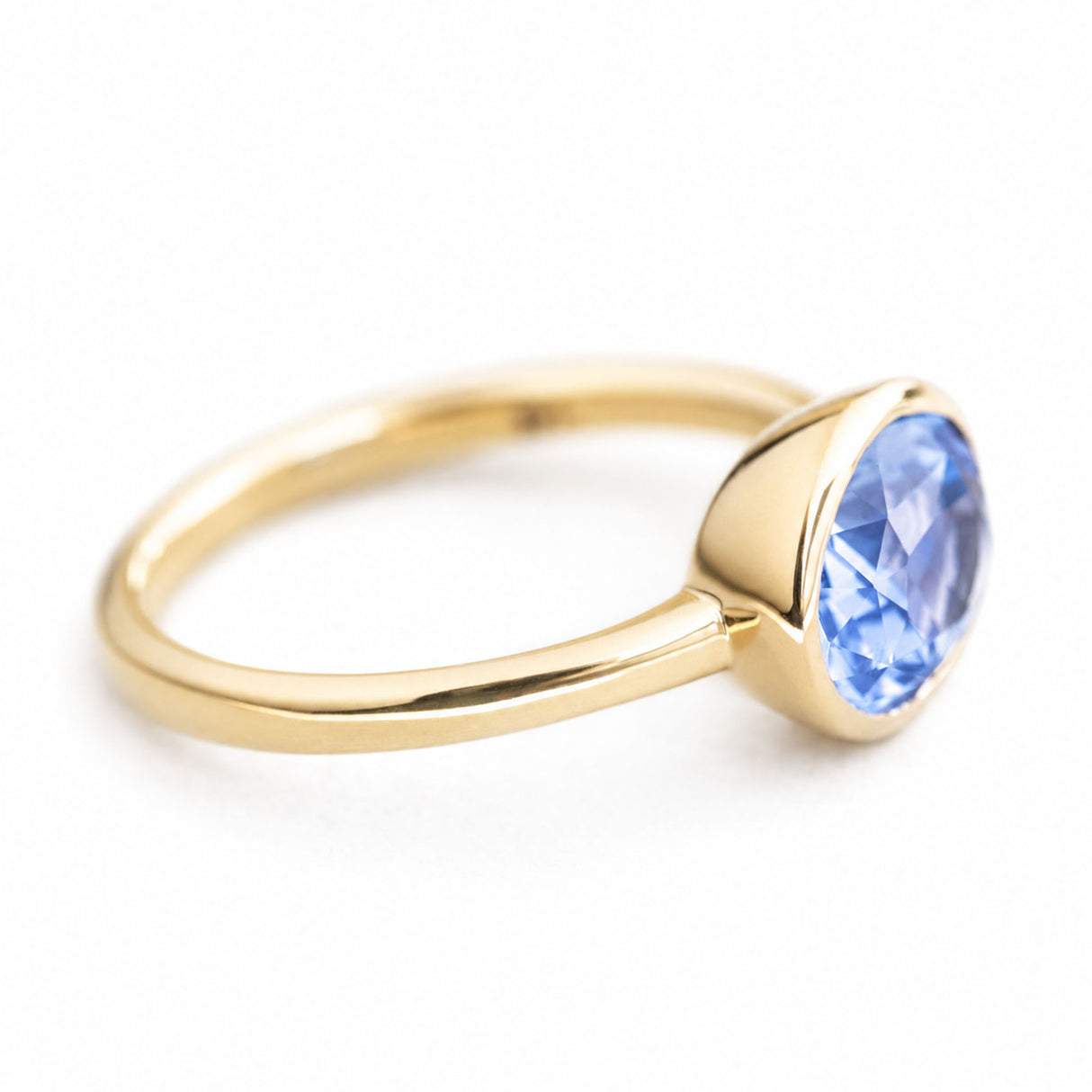 A three-quarter close-up of an antique-inspired engagement ring with ablue oval sapphire set in 14ct yellow gold.