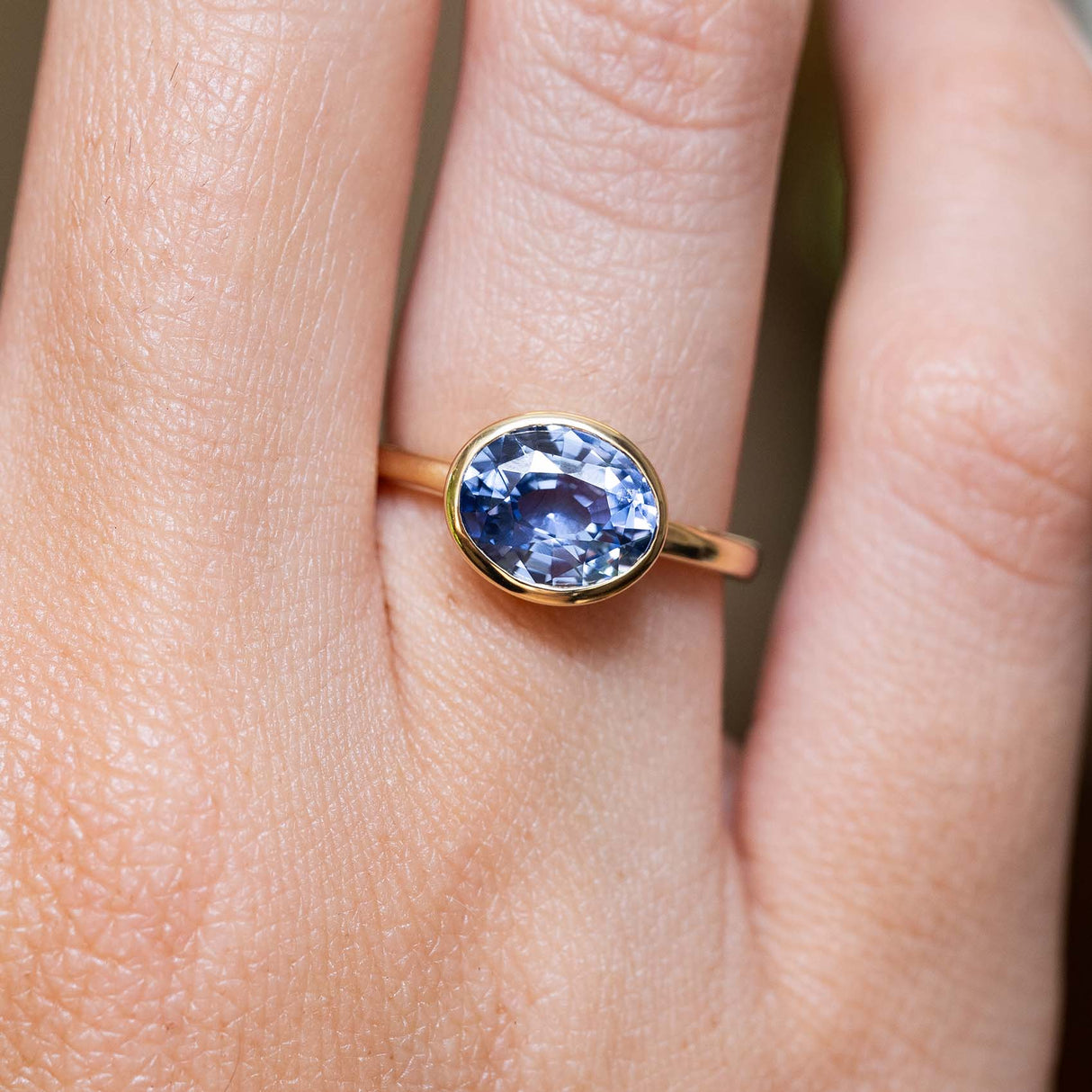 An antique-inspired blue sapphire solitaire ring in yellow gold worn on the finger.