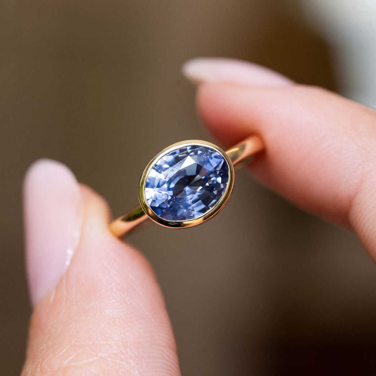 Close detail of an antique-inspired oval-cut blue sapphire solitaire ring in yellow gold held between fingers.
